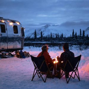 Couple enjoying a fire outside of their RV surrounded by snow